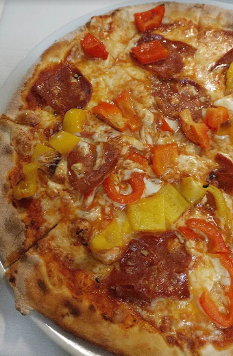 Primo piano di una pizza condita con formaggio fuso, pomodori rossi, peperoni gialli e carne rosolata su un piatto bianco.
