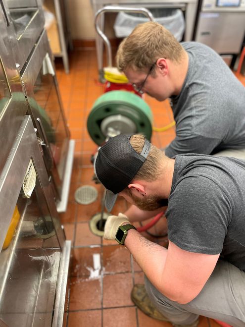 A plumber is kneeling on the floor fixing a sink in a kitchen.