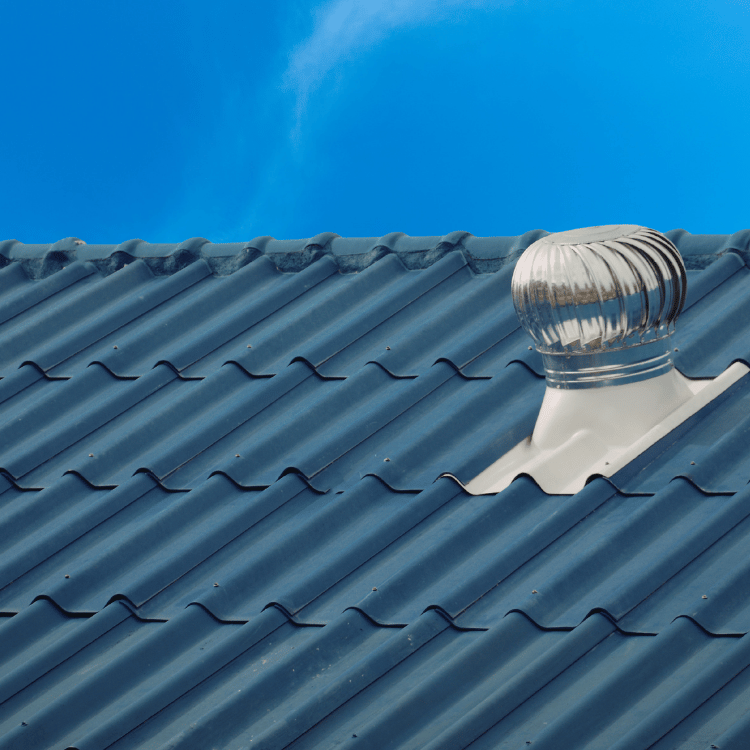 Blue tiled roof with a spinning metal wind turbine against a bright blue sky.