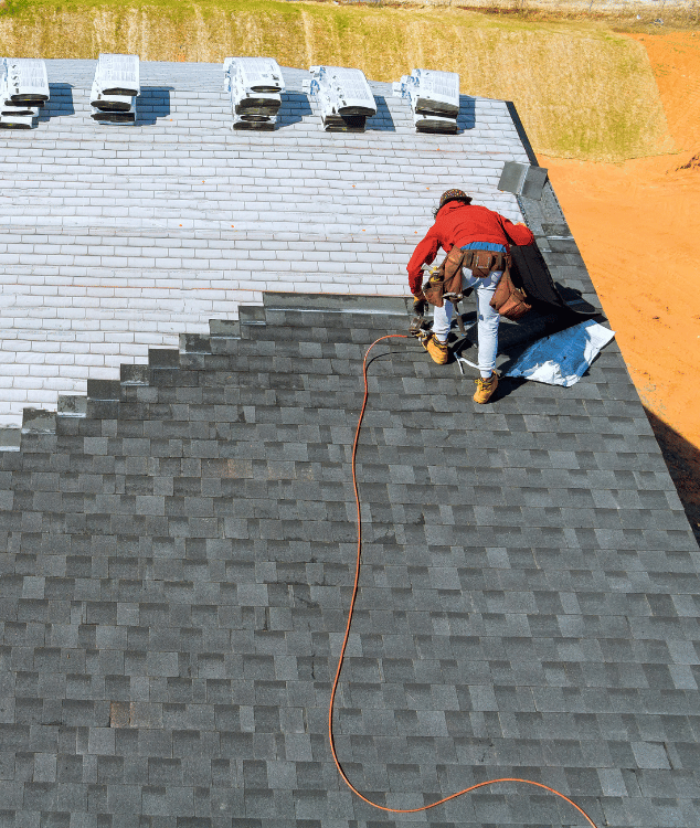 Roofer installing shingles on a roof; gray and black shingles, person in red jacket, daylight.
