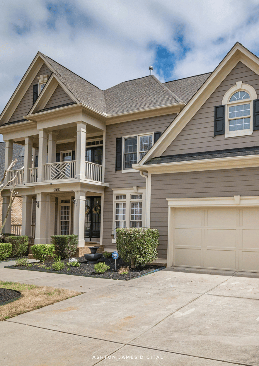 Two-story house with gray siding, columns, and a garage on a sunny day.