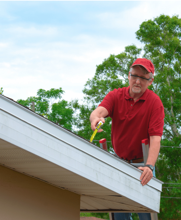 Man on a ladder measuring a house gutter with a tape measure.