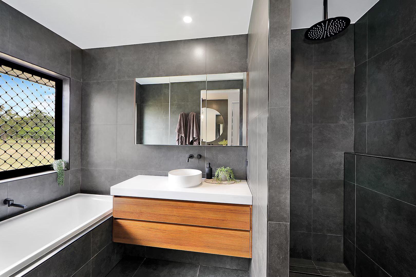 Modern bathroom with gray tiled walls, wooden vanity, and shower.