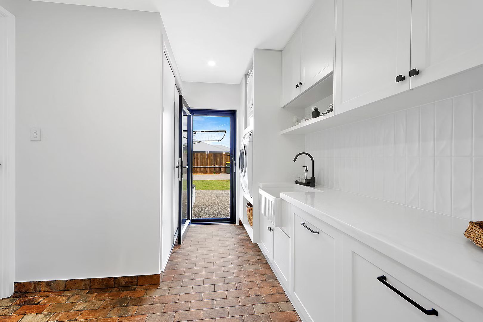 Laundry room with white cabinets, brick floor, and doorway to the outdoors.