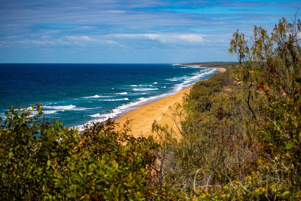 A Sandy Beach Stretches Along a Coastline Under a Blue Sky — Master Cabinets Bundaberg in Agnes Water, QLD