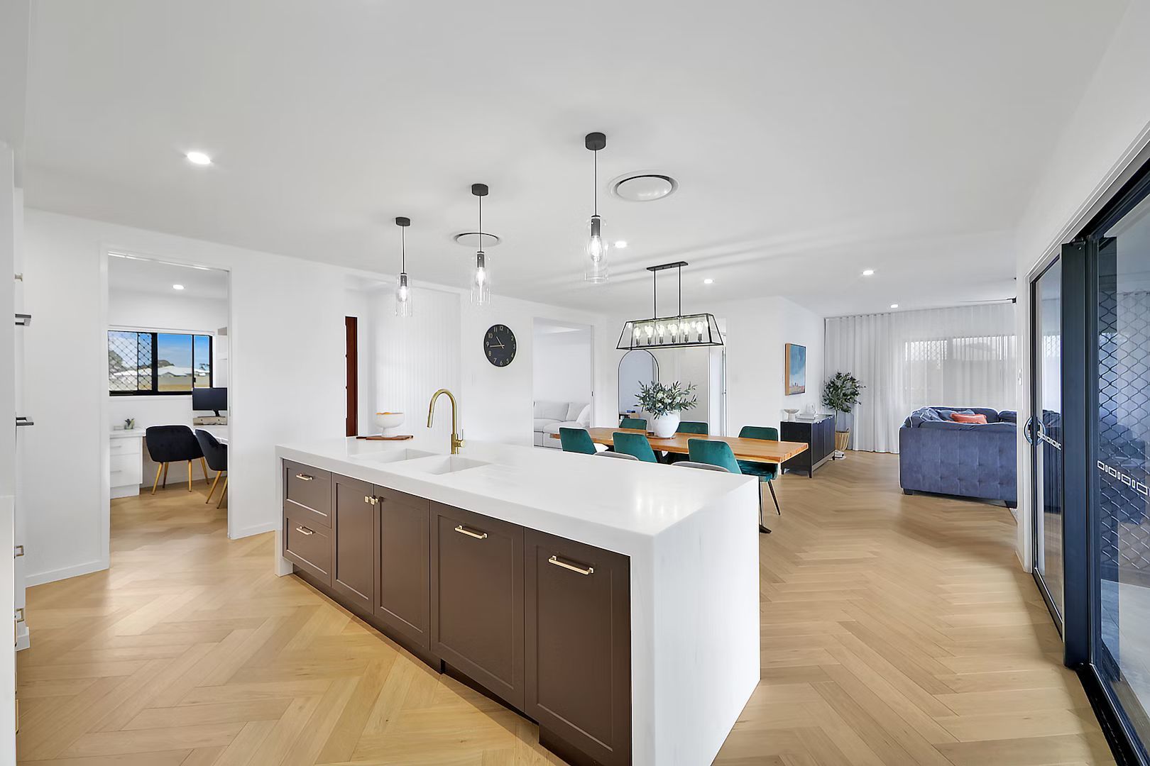 Open-plan kitchen and living space with white walls, island, wooden floor, and sliding glass door.