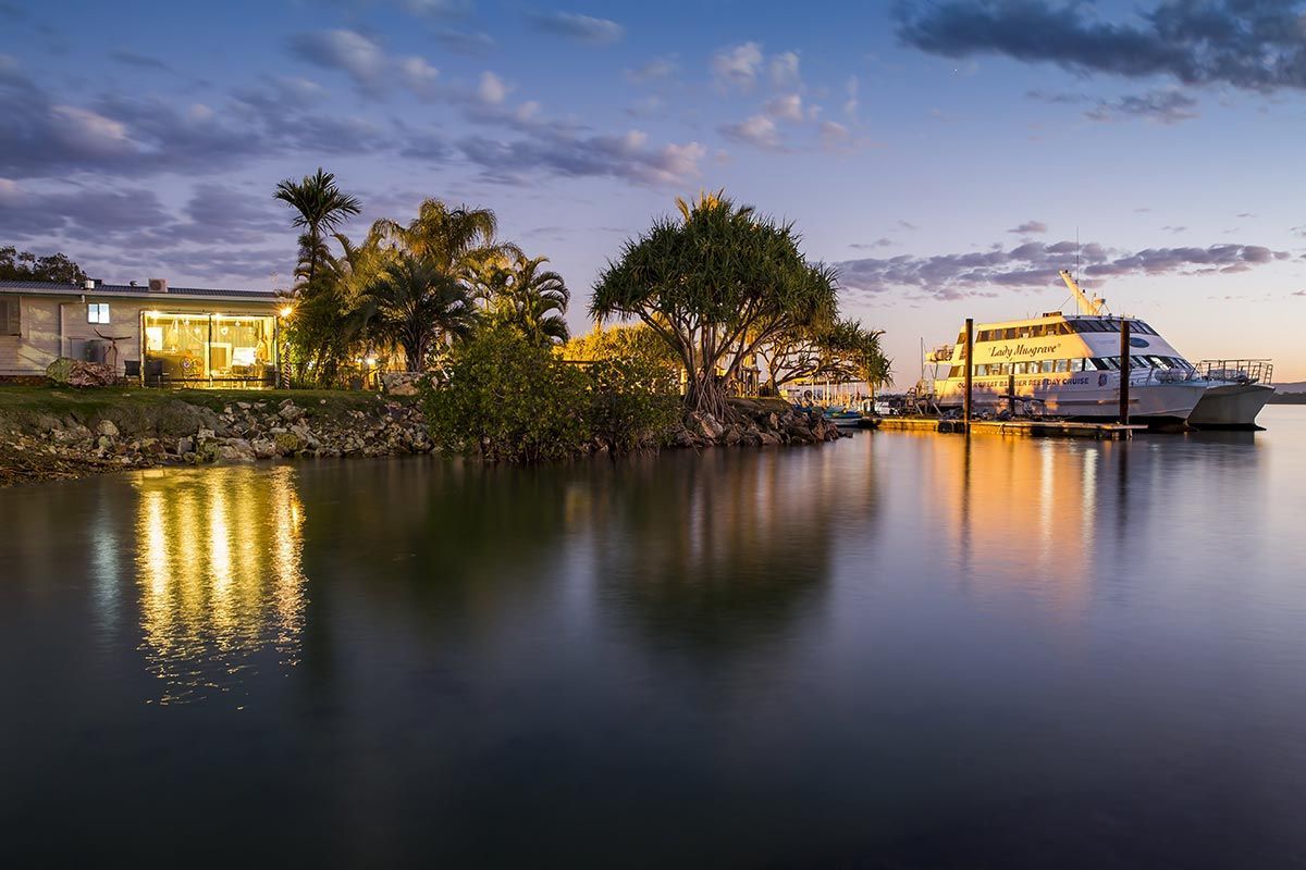 A Boat Is Docked In The Water Near A House — Master Cabinets Bundaberg in Redridge, QLD