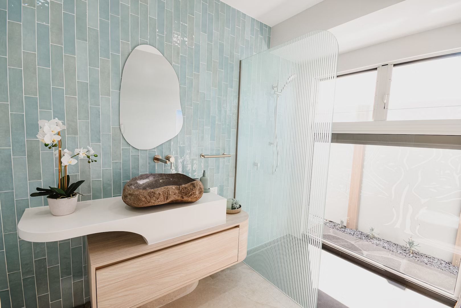 Modern bathroom with light blue tile walls, stone sink, and frosted glass shower door.