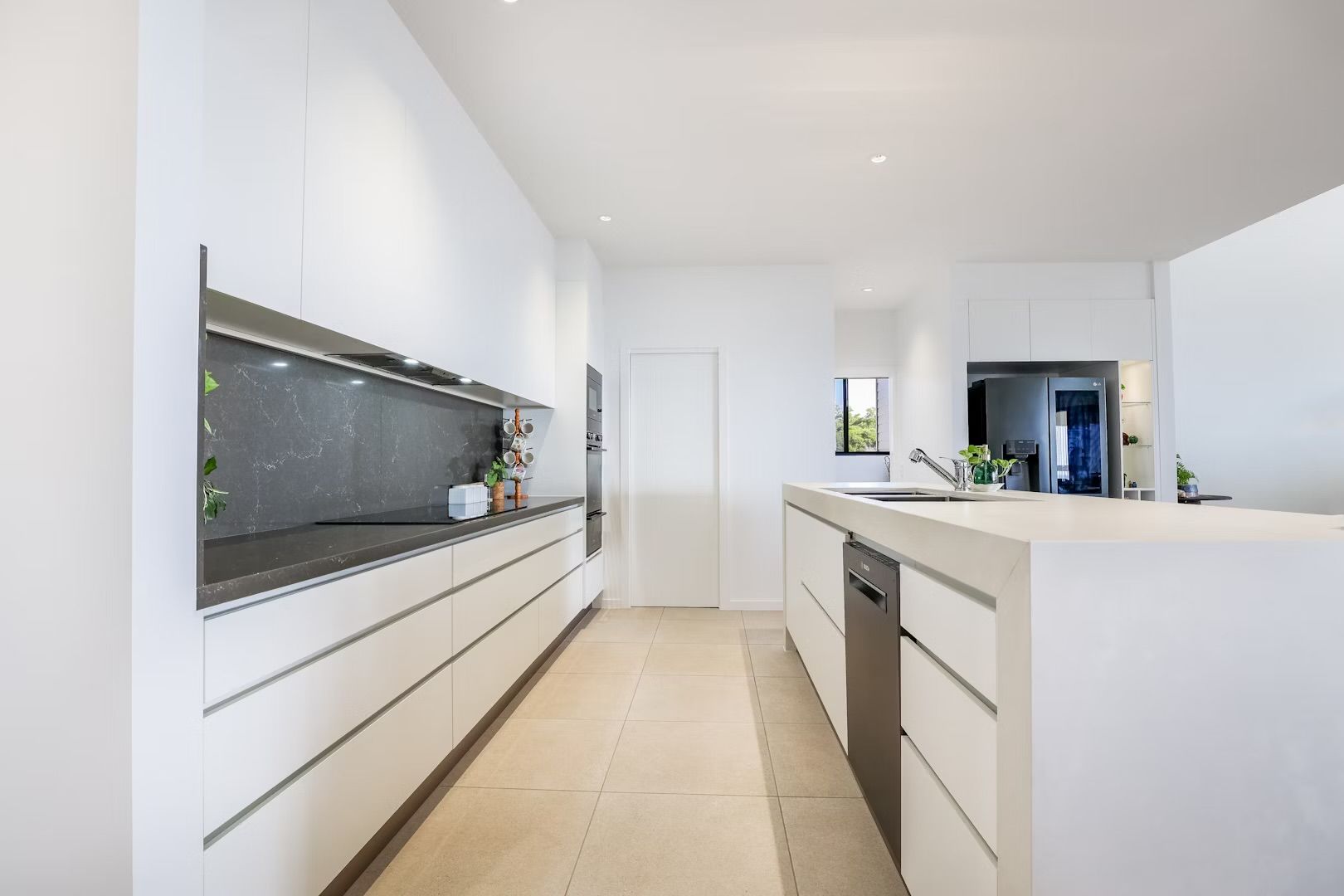 Modern white kitchen with long counter and island. Stainless steel dishwasher.