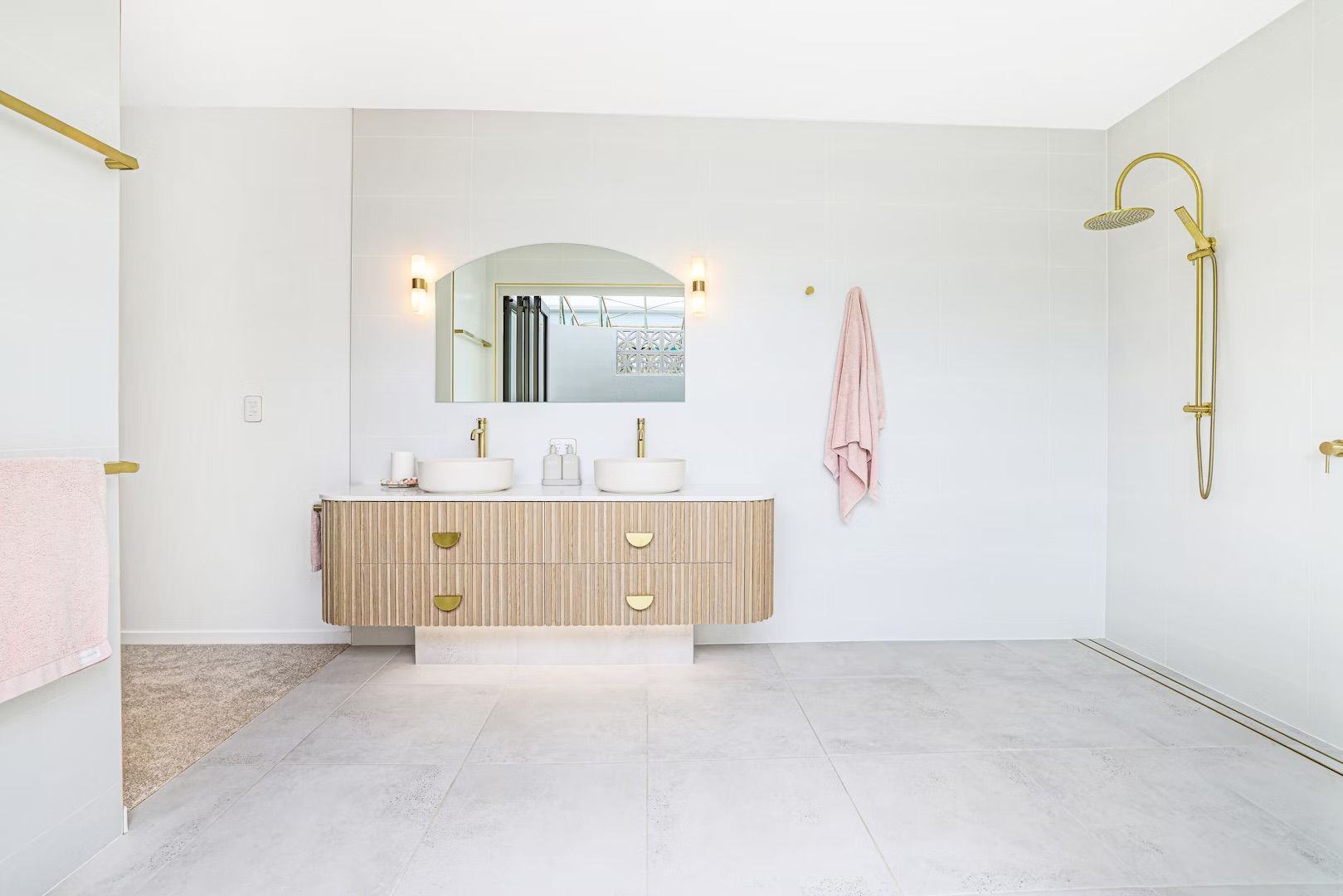 Modern bathroom with light wood vanity, round sinks, gold fixtures, and a large mirror.
