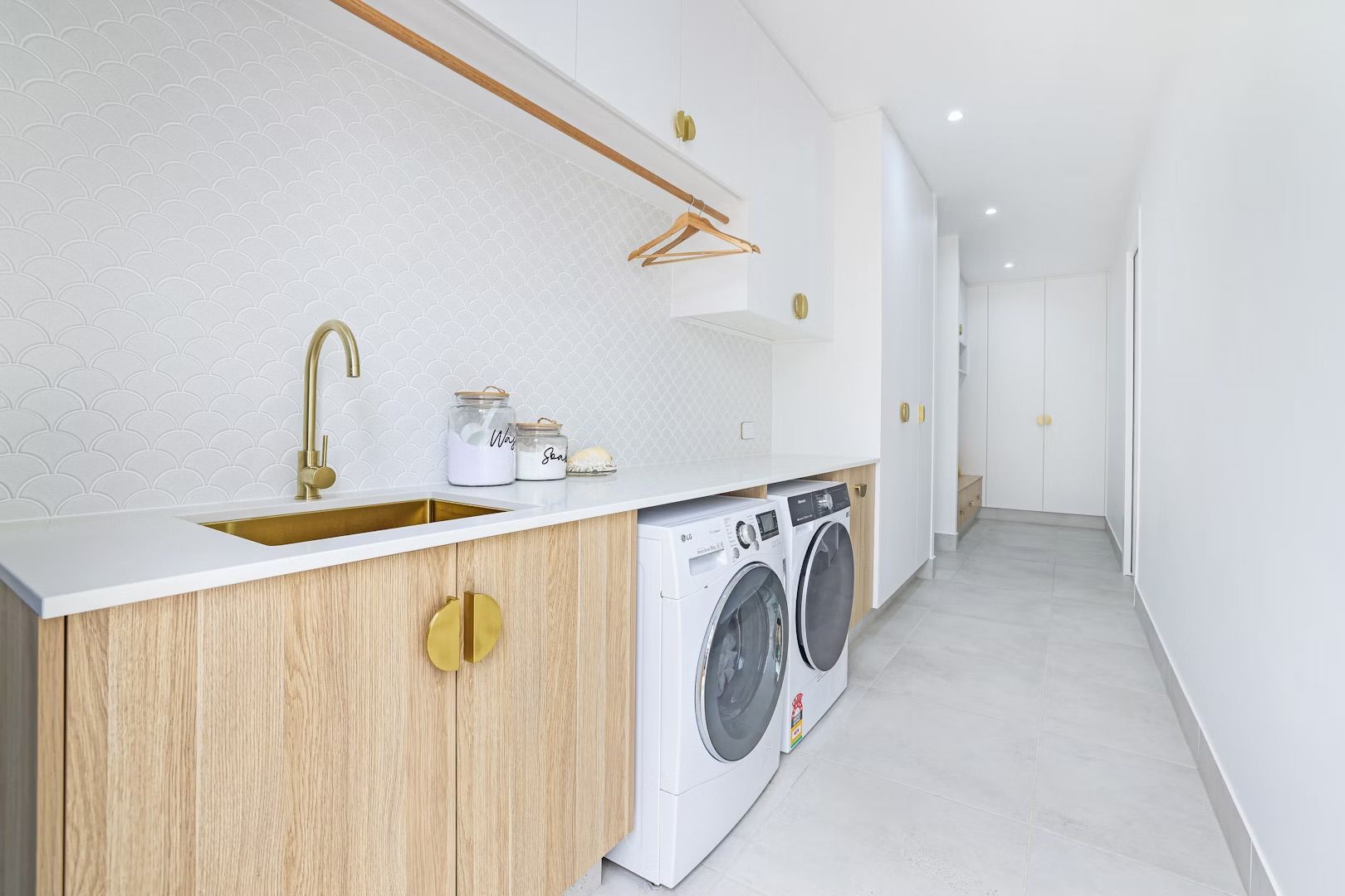 Laundry room with a washing machine, sink, and storage cabinets. Gold fixtures and white walls.