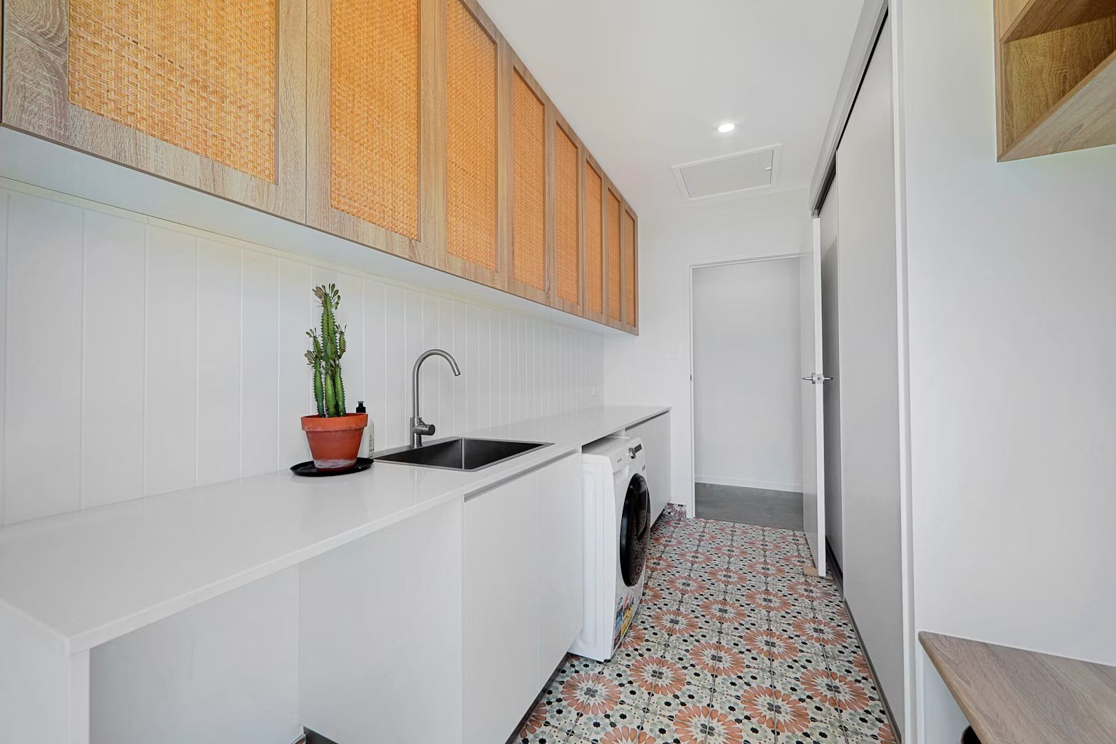 Laundry room with white cabinets, wicker overhead storage, sink, and patterned floor tiles.