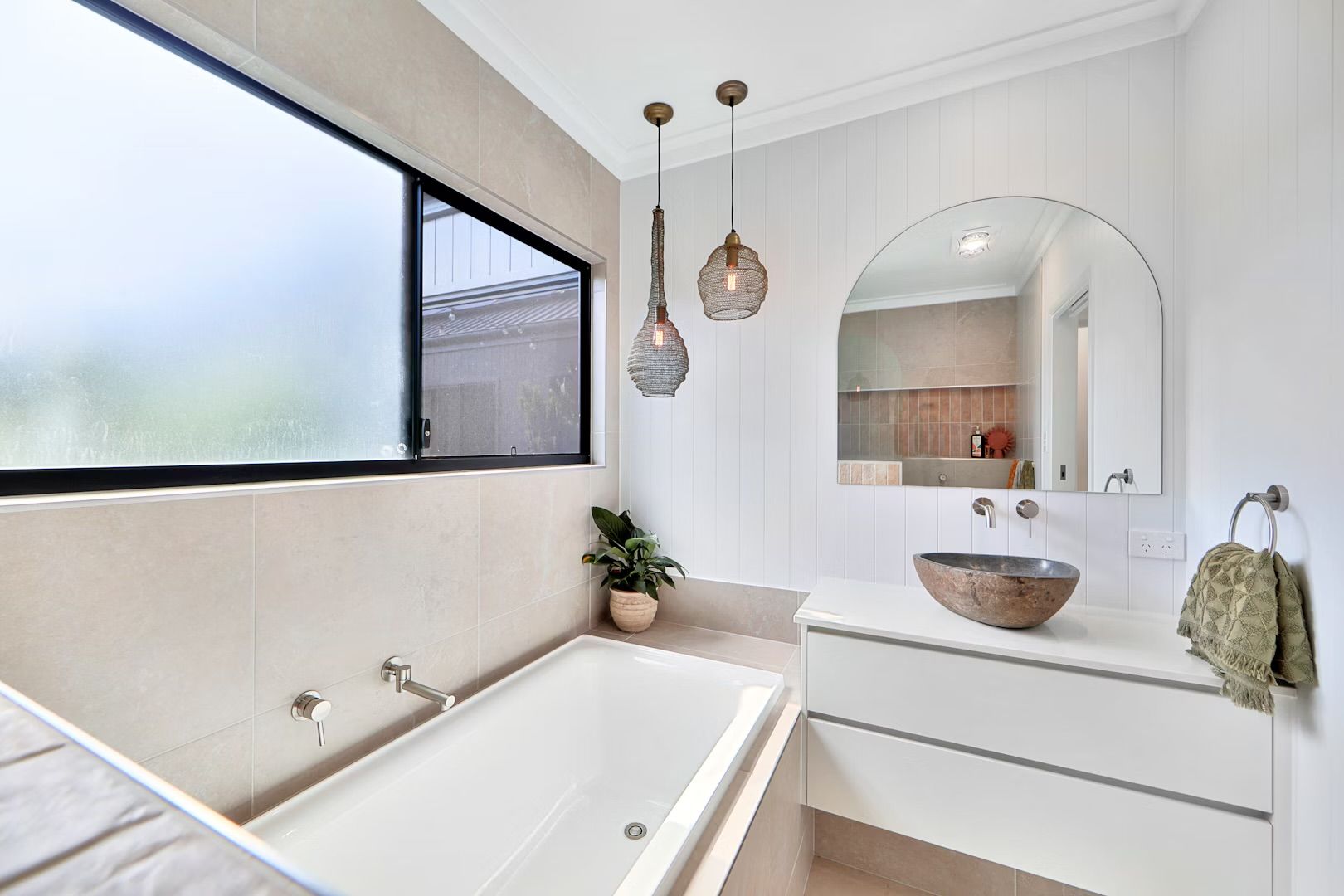 Bathroom with bathtub, sink, and large window. Two hanging pendant lights above.