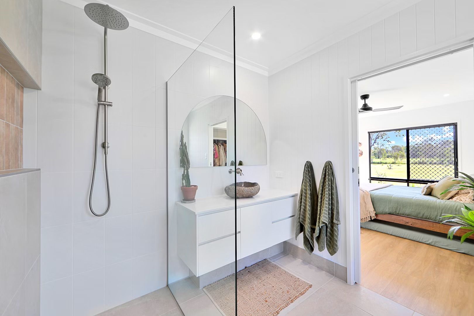 Modern bathroom with white walls, shower, vanity, and open doorway to a bedroom.