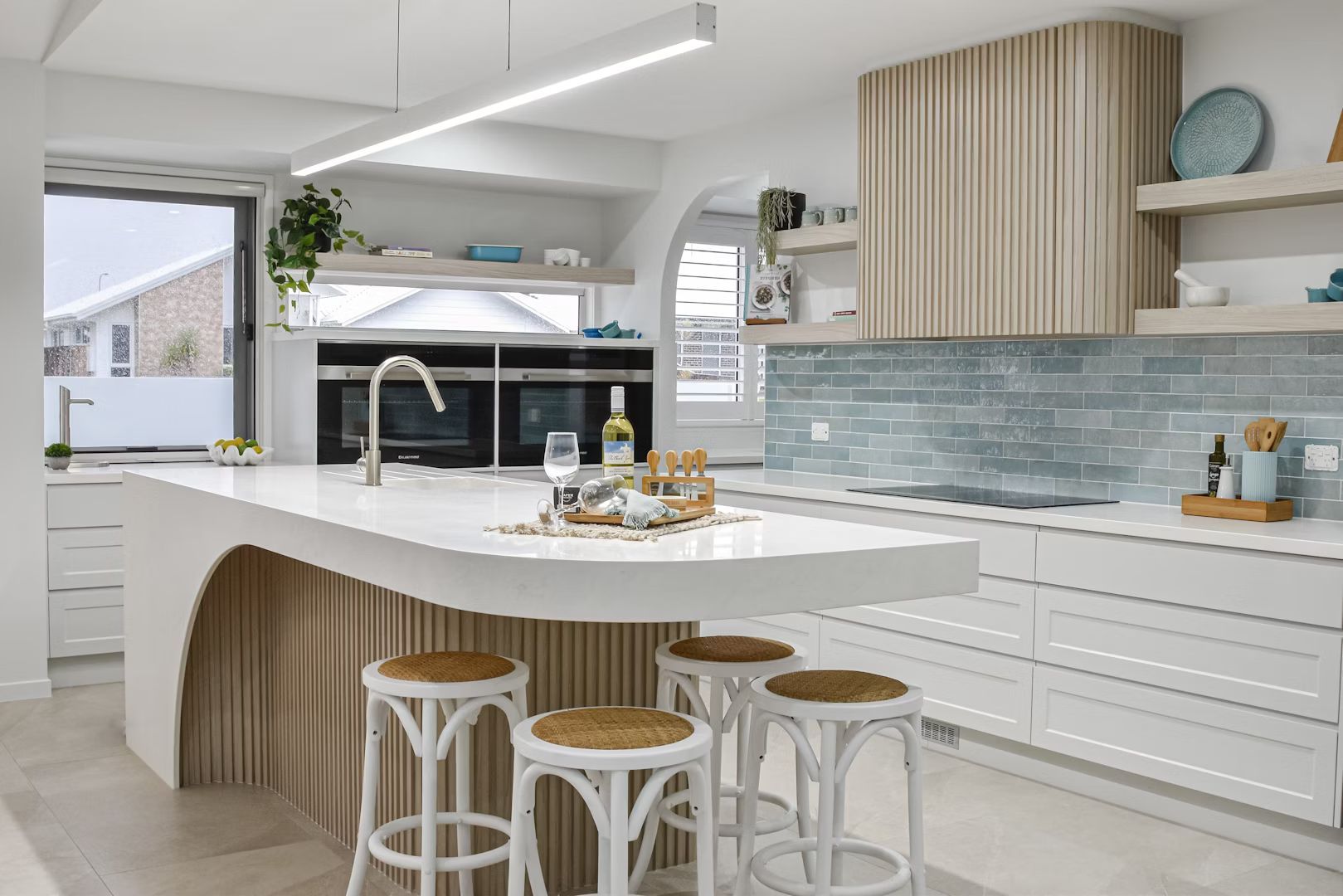 Modern white kitchen with a curved island, wooden accents, and bar stools.