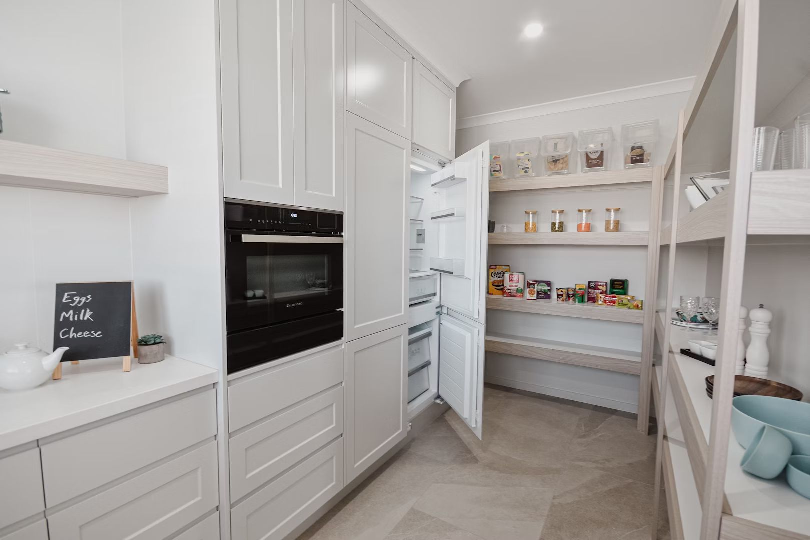 Kitchen with light gray cabinets, open refrigerator, and pantry with shelves filled with food.