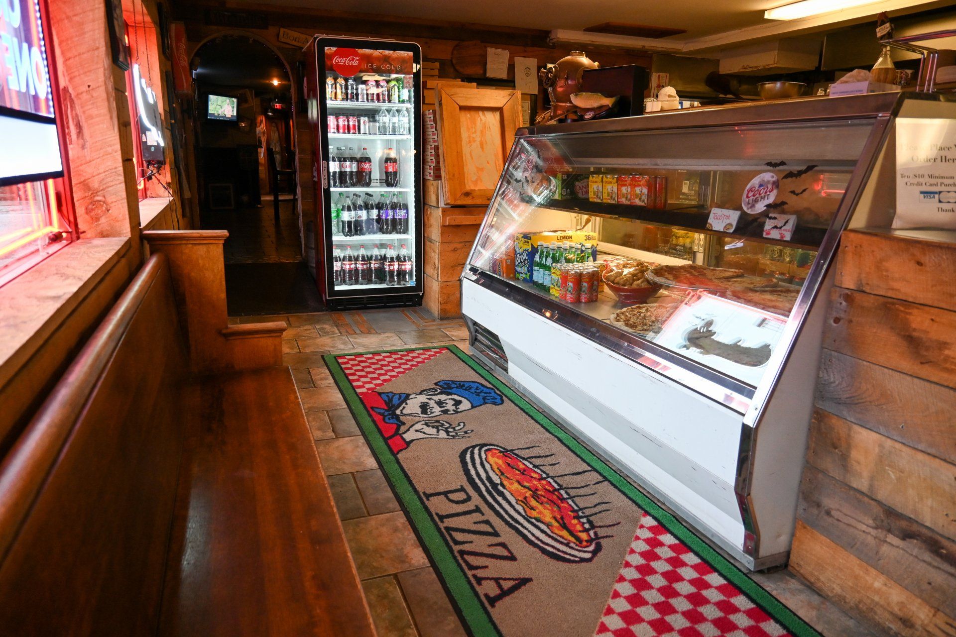 A pizza display case in a restaurant with a rug that says pizza on it