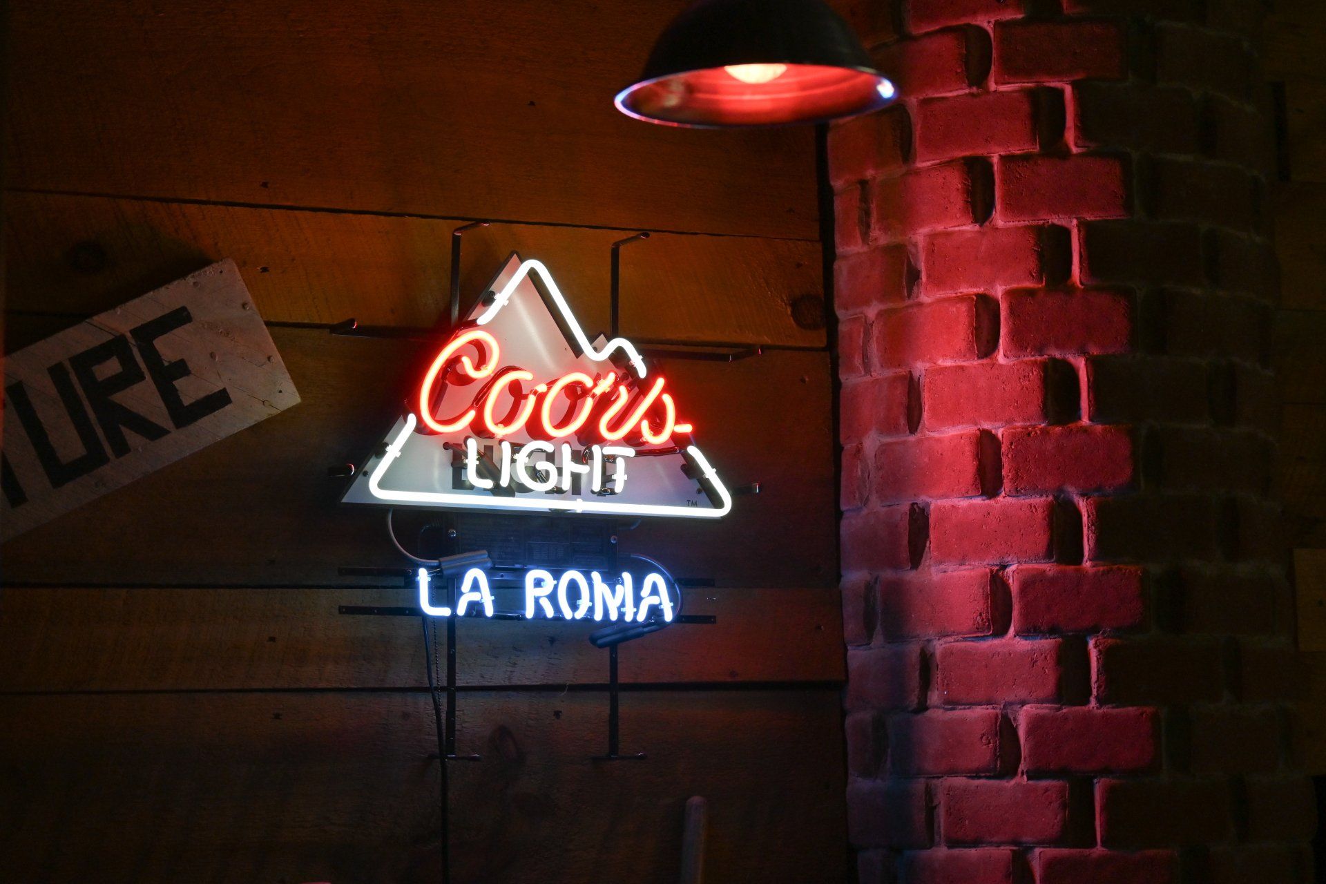 A neon sign for coors light hangs on a brick wall
