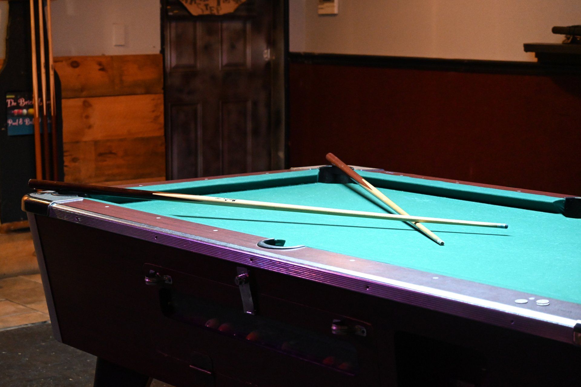 A pool table with two cues on it in a room