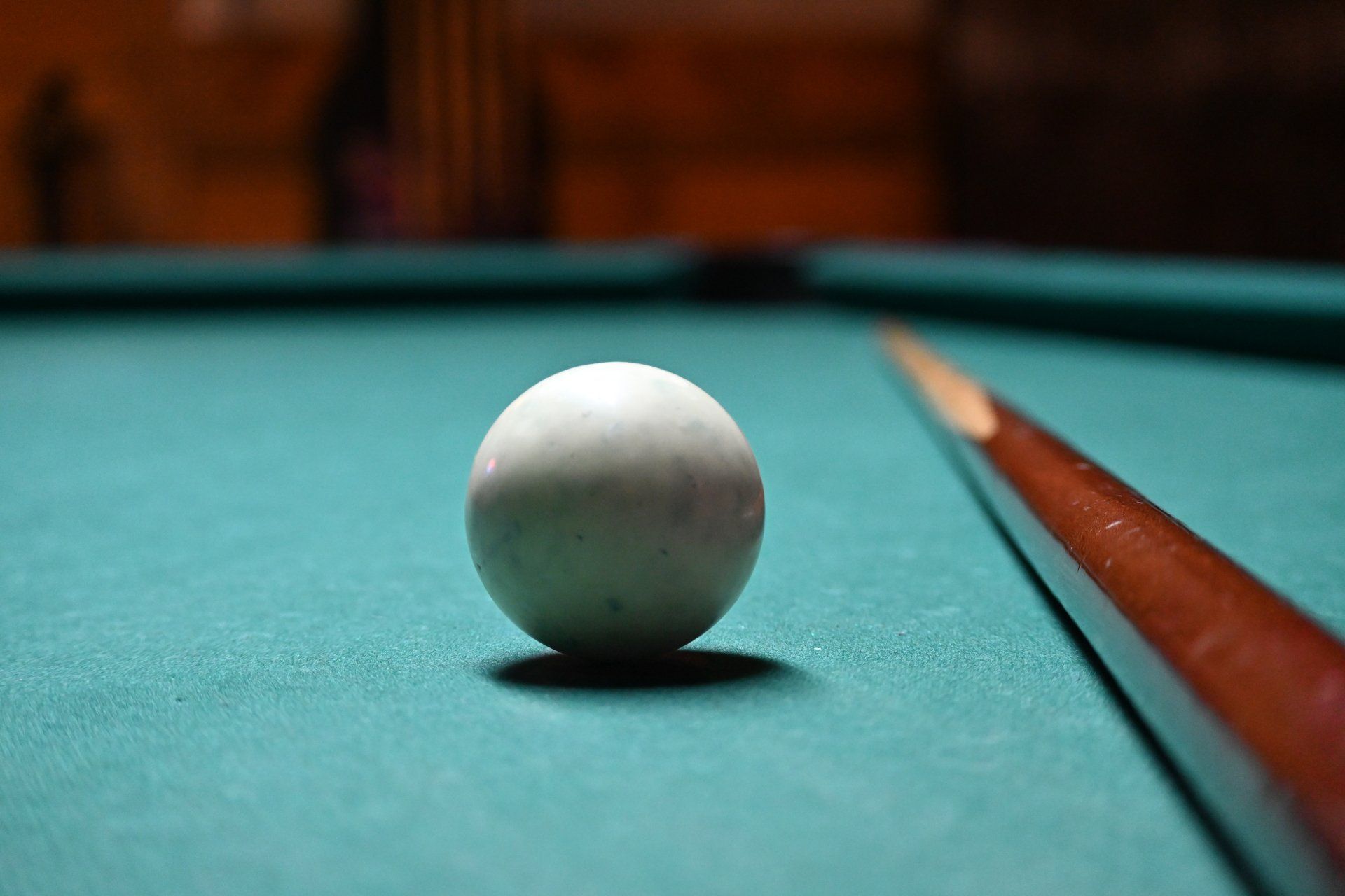 A pool ball is sitting on a pool table next to a cue.