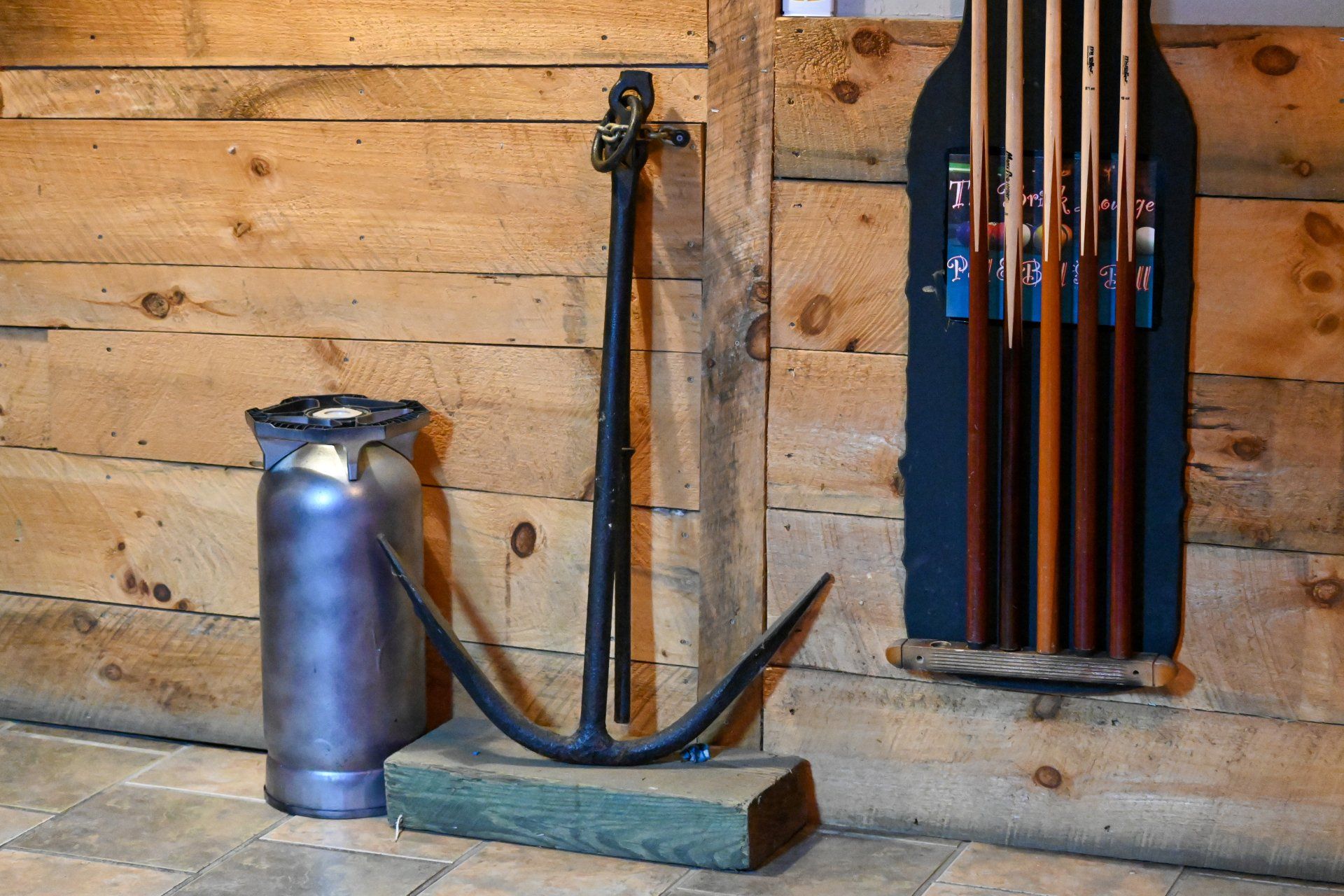 An anchor is leaning against a wooden wall next to a milk can.