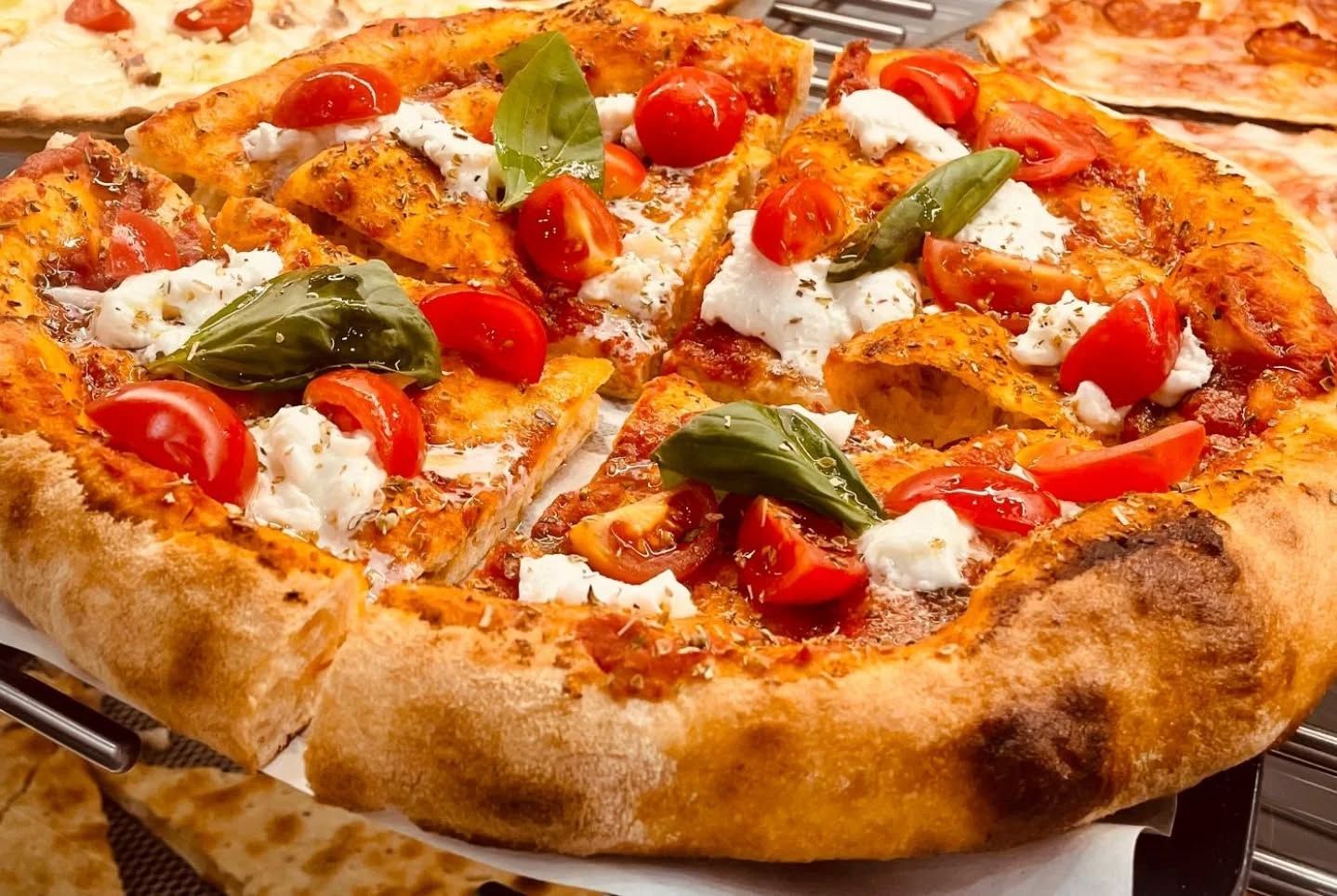 Pizza condita con pomodori, basilico e formaggio; primo piano.