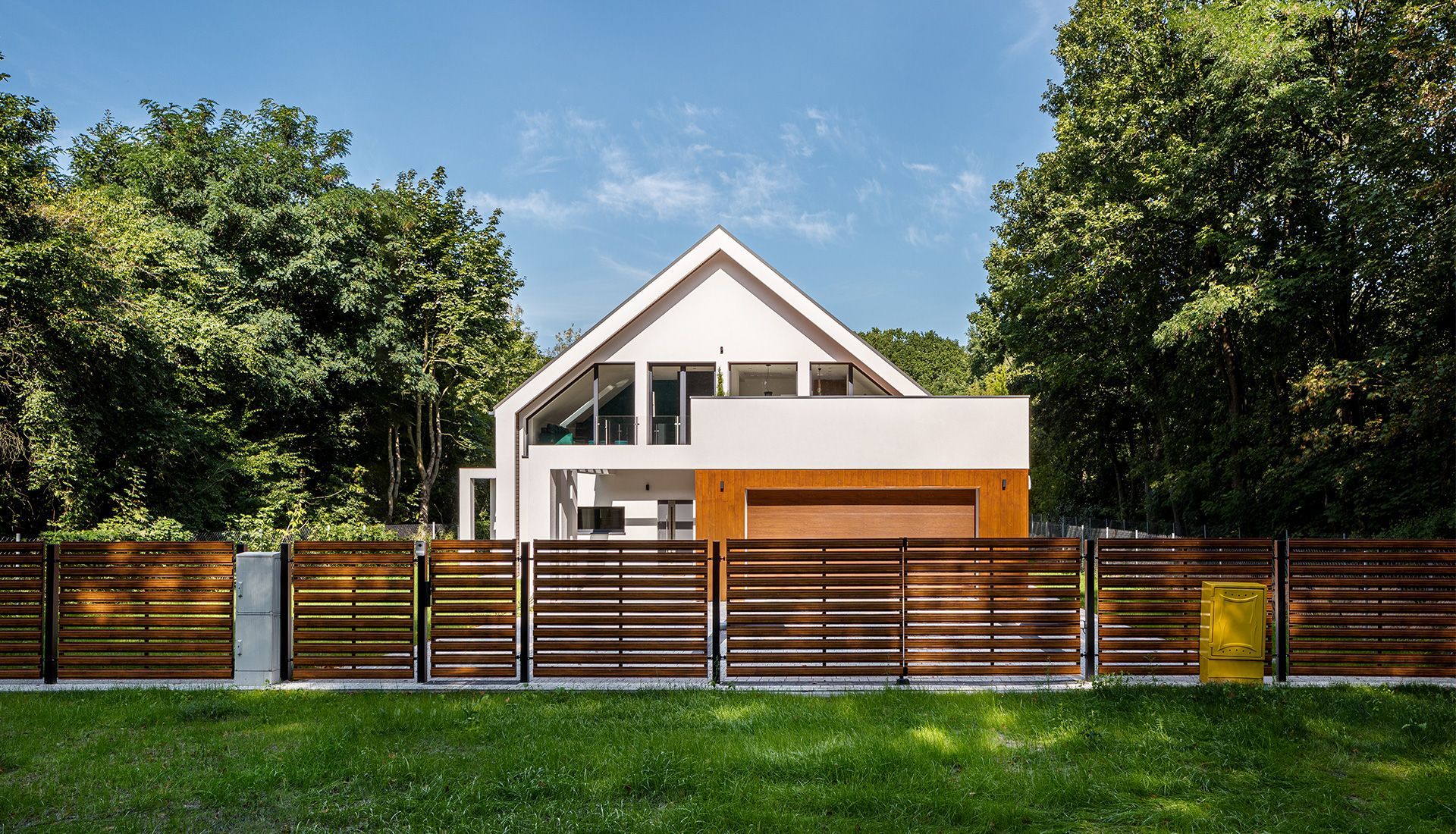 White modern house with wooden fence, surrounded by green trees and grass.