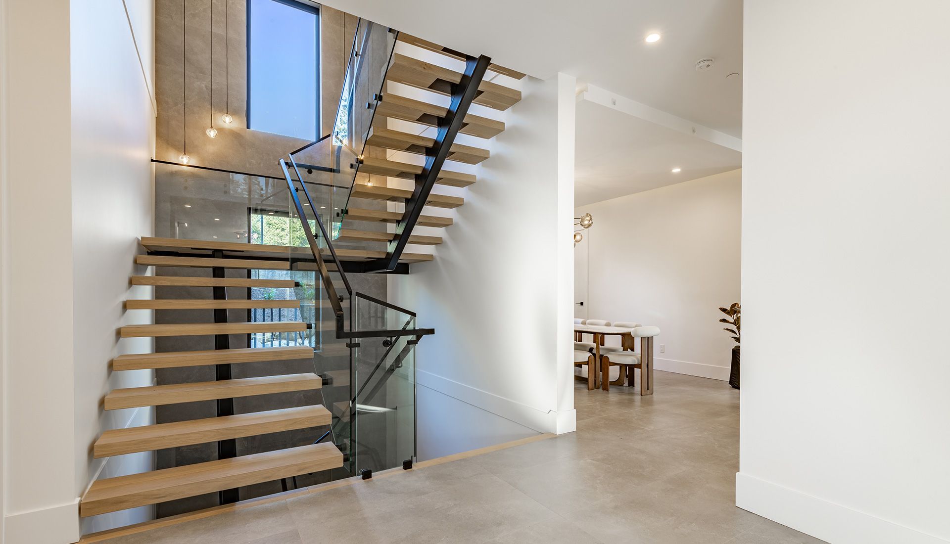 Interior view: Modern staircase with wooden steps, black railing, concrete wall, and adjacent dining area.