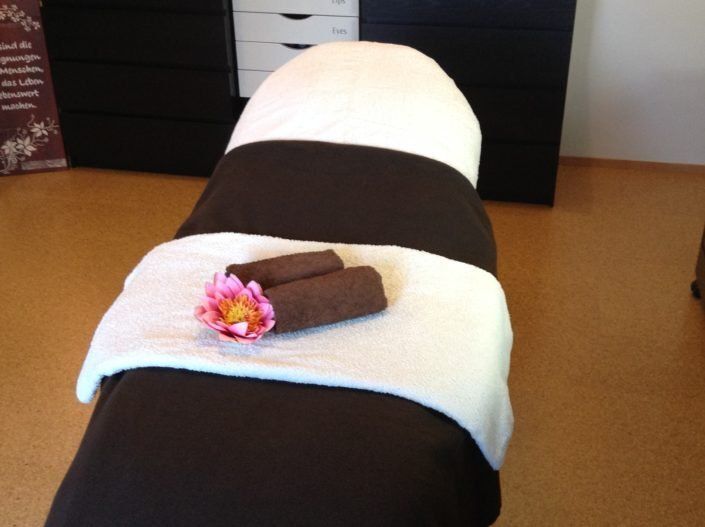 Ein Massagetisch mit Handtüchern und einer Blume darauf