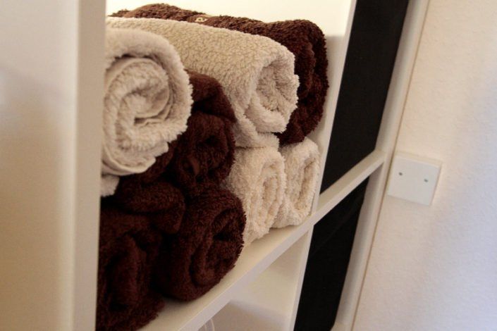 Braune und weiße Handtücher liegen aufgerollt auf einem Regal