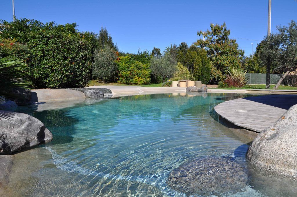 Piscina color turchese e trasparente circondata da rocce, vegetazione e una terrazza in legno sotto un cielo azzurro.