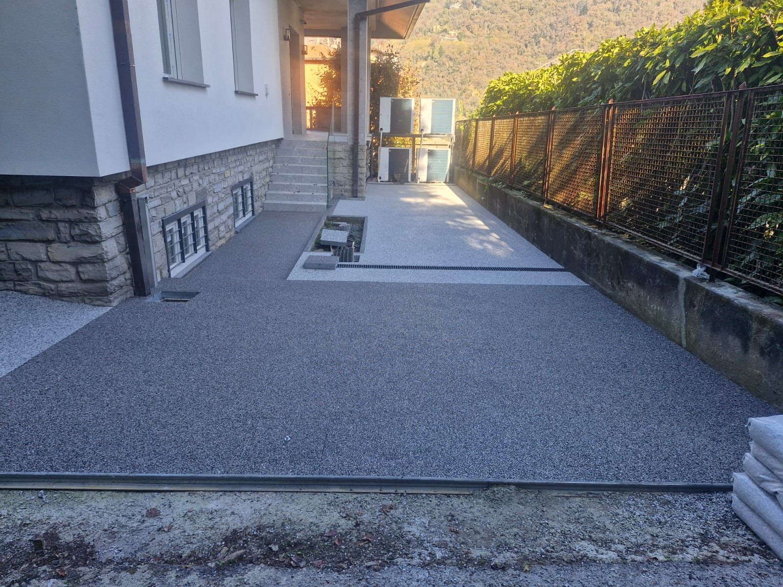 Area esterna ricoperta di ghiaia accanto a un edificio con gradini e recinzione.