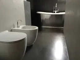 Bagno moderno con WC e bidet bianchi, vasca da bagno argentata, pavimento scuro e termosifone.