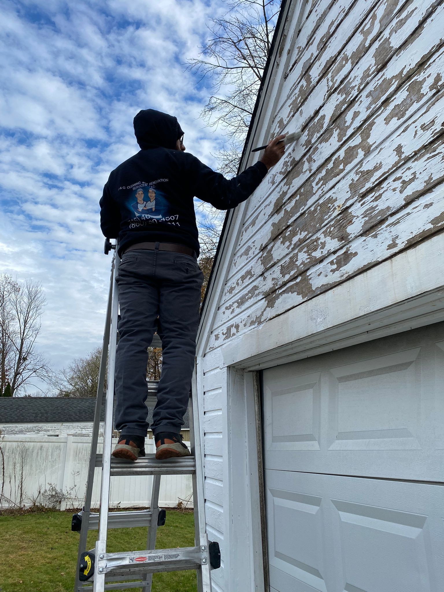 A man is standing on a ladder painting a garage door.