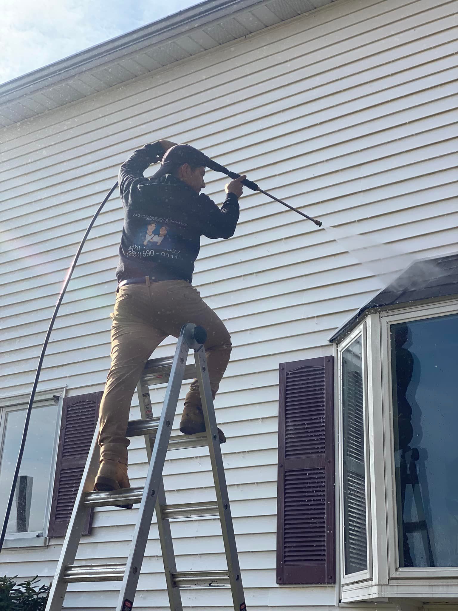 A man in a yellow raincoat is cleaning a white fence with a hose.