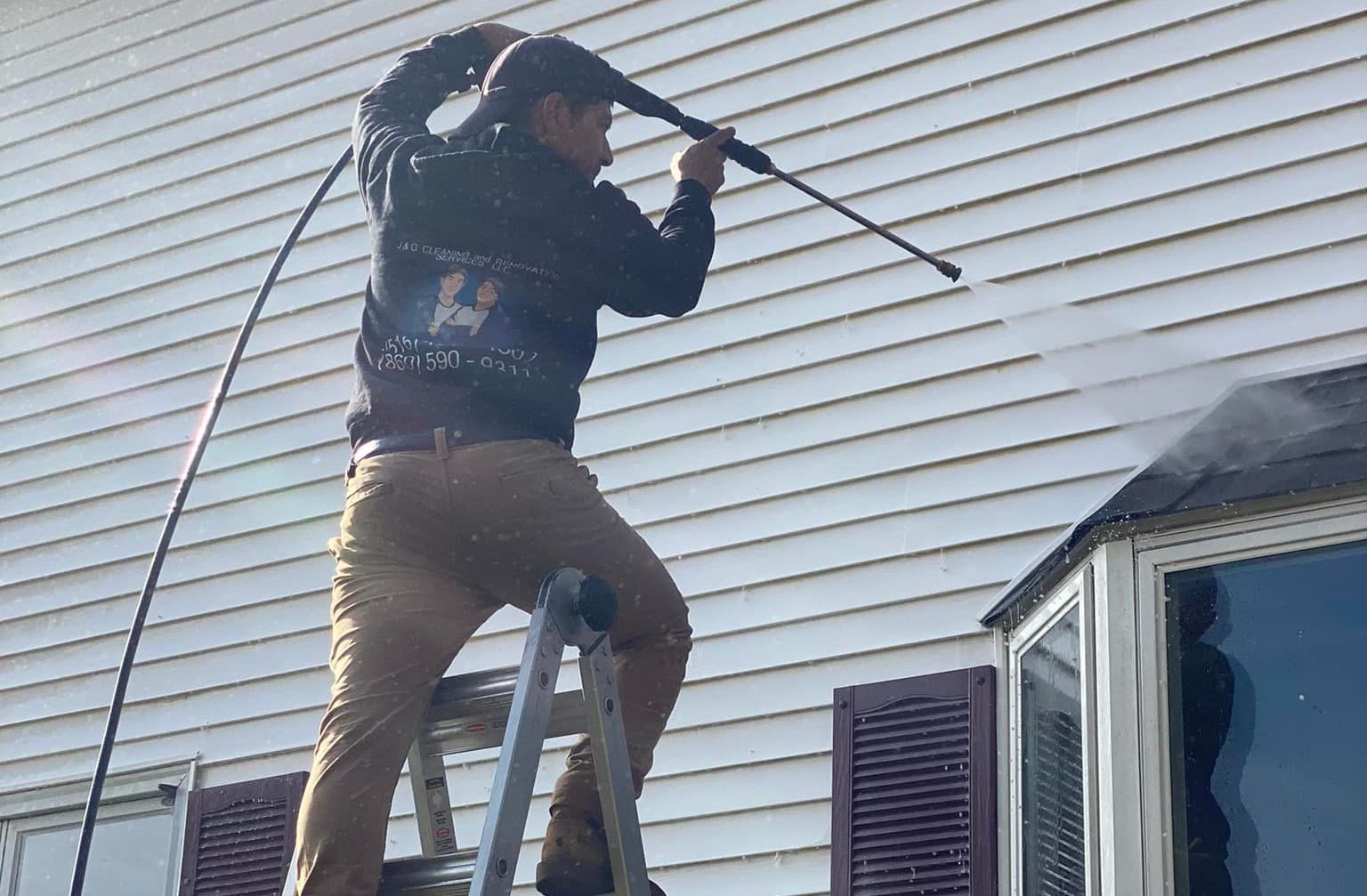 A man is standing on a ladder painting a garage door.