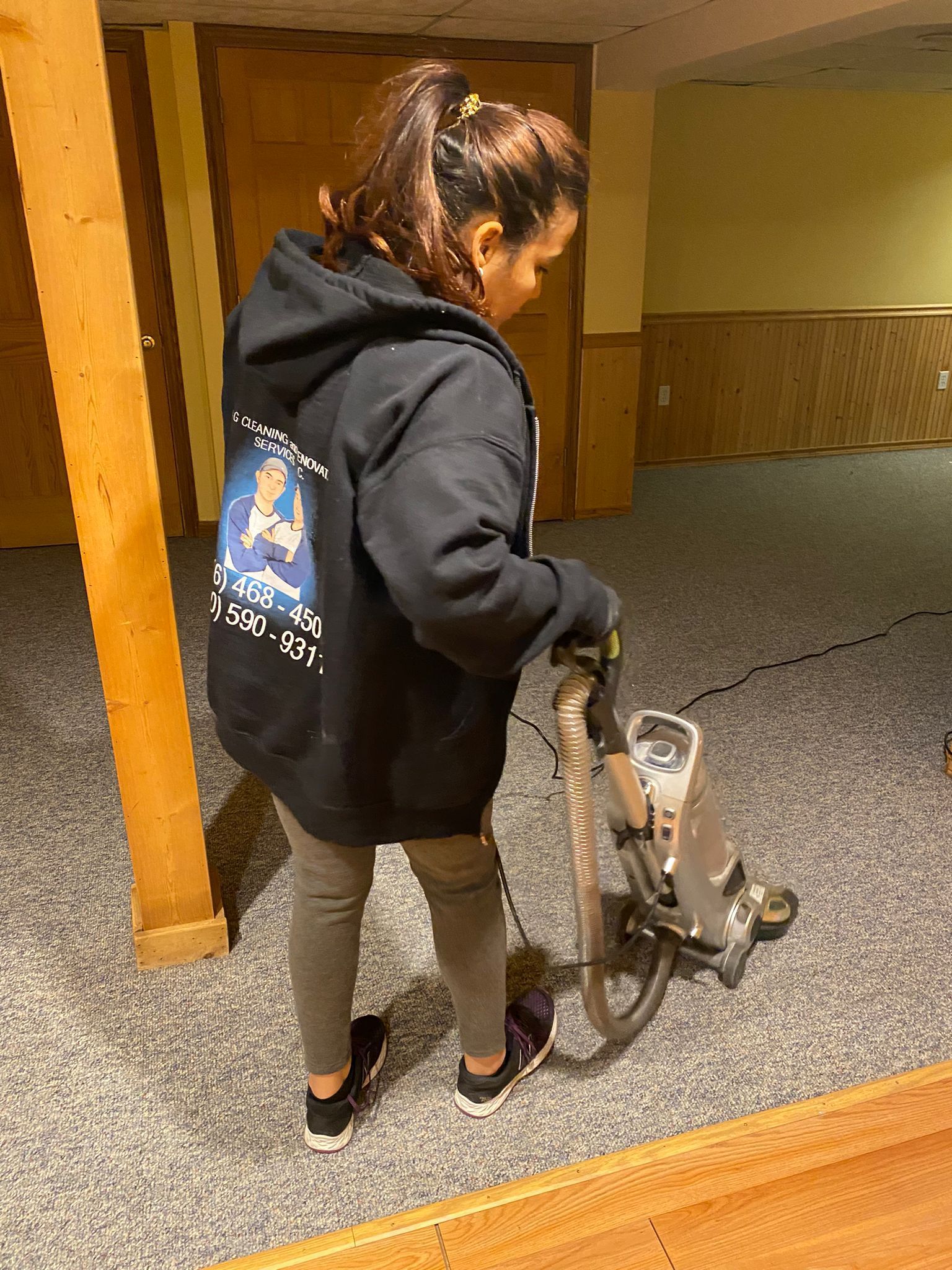 A woman is using a vacuum cleaner to clean a carpet in a basement.