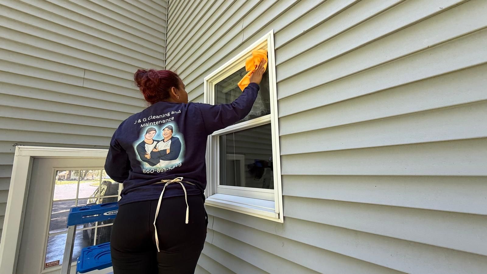 A man is standing on a ladder painting a garage door.