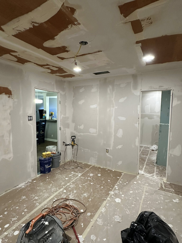 Room with drywall; tools and supplies on the floor; two doorways; overhead lights.