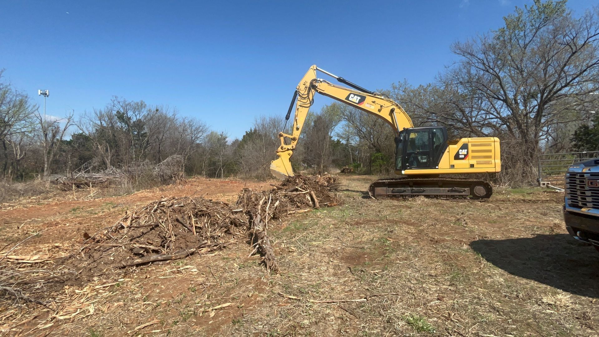 A yellow excavator clears brush and debris from a field on a sunny day.
