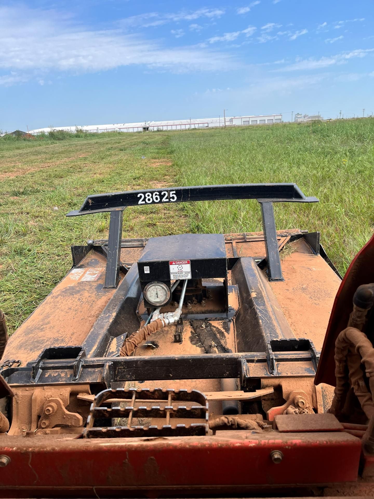A view from a tractor looking over a red rotary cutter in a field, with a black metal support labeled 