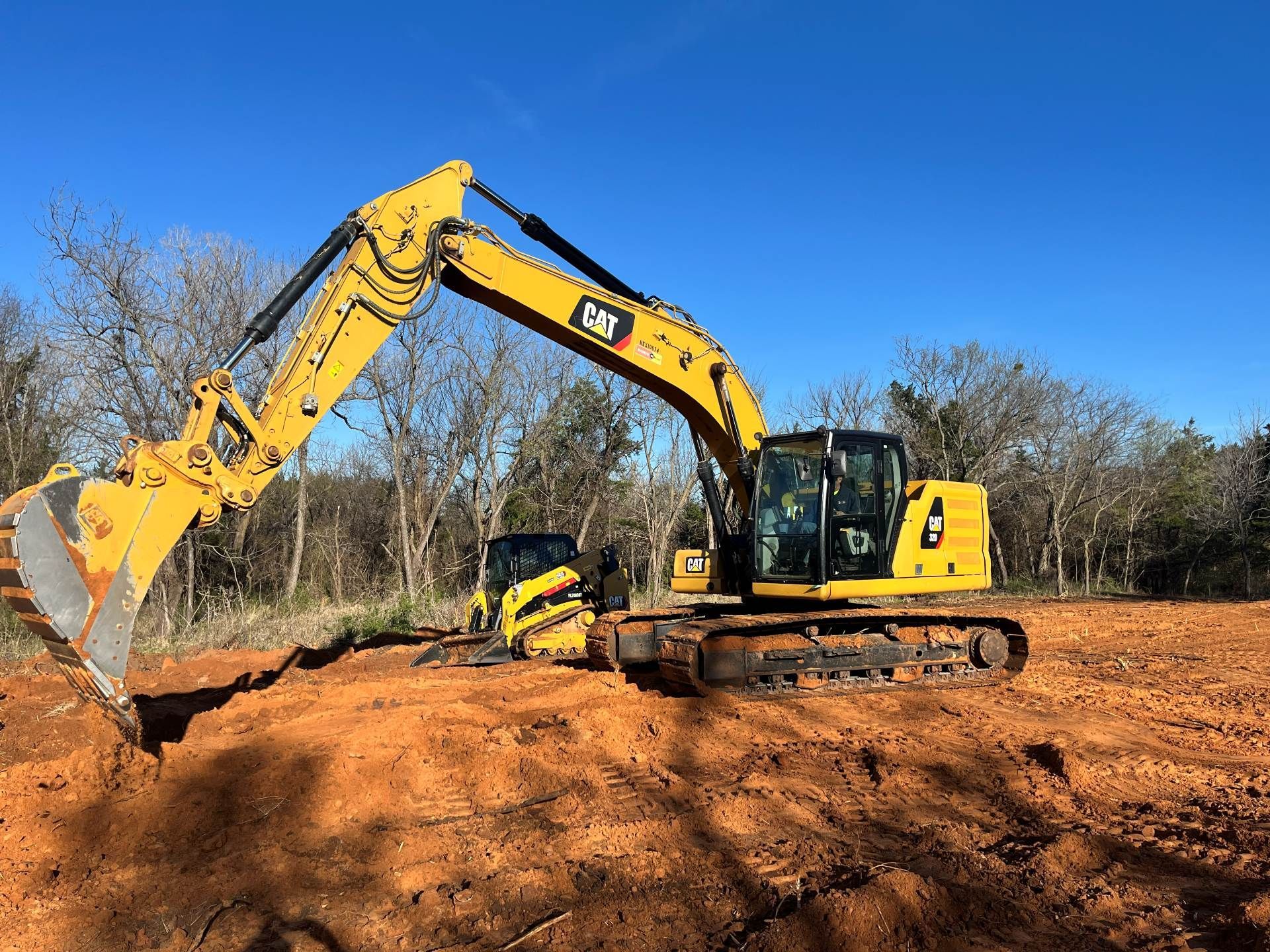 A bright yellow Caterpillar excavator sits on a dirt construction site against a clear blue sky.