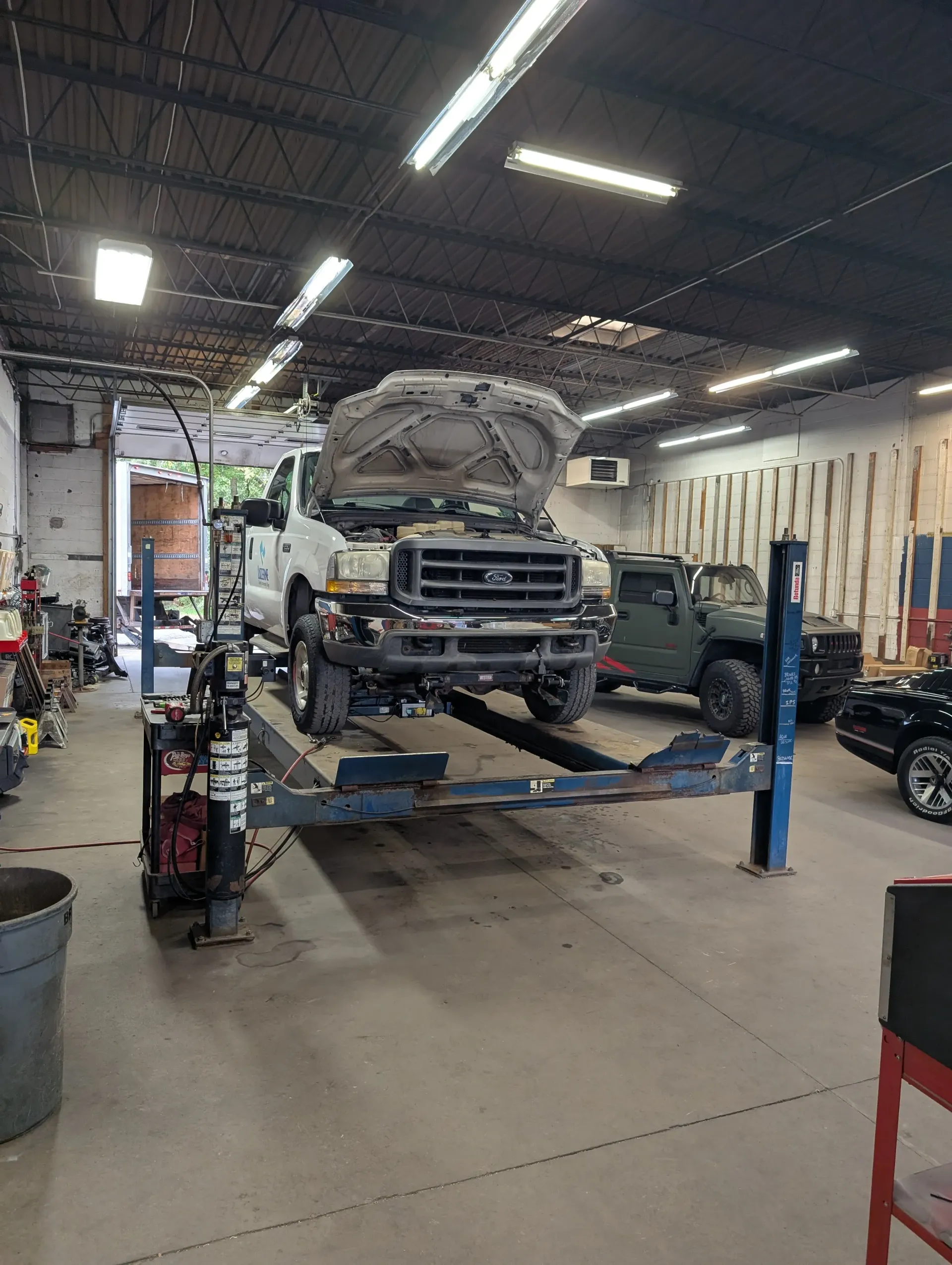 White truck raised on a hydraulic lift inside an auto repair shop with the hood open | Rymer Automotive