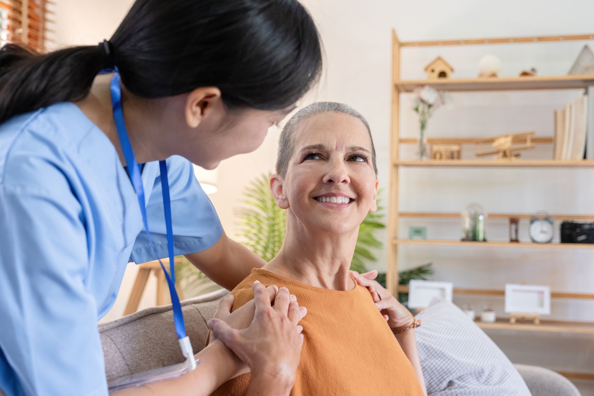 A nurse is helping an elderly woman sit on a couch.