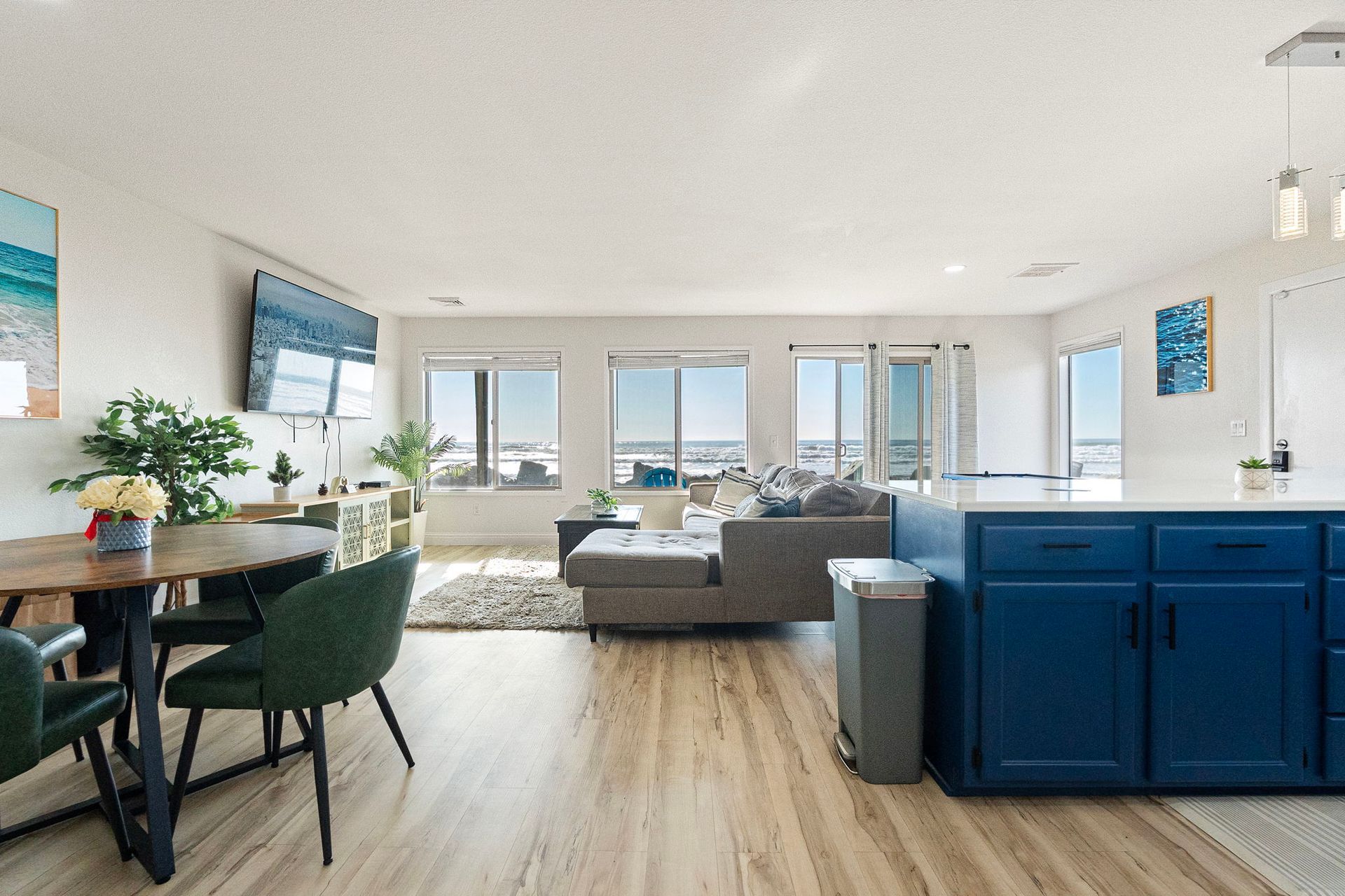 Bright living space with gray sectional sofa, blue cabinets, and light wood flooring.