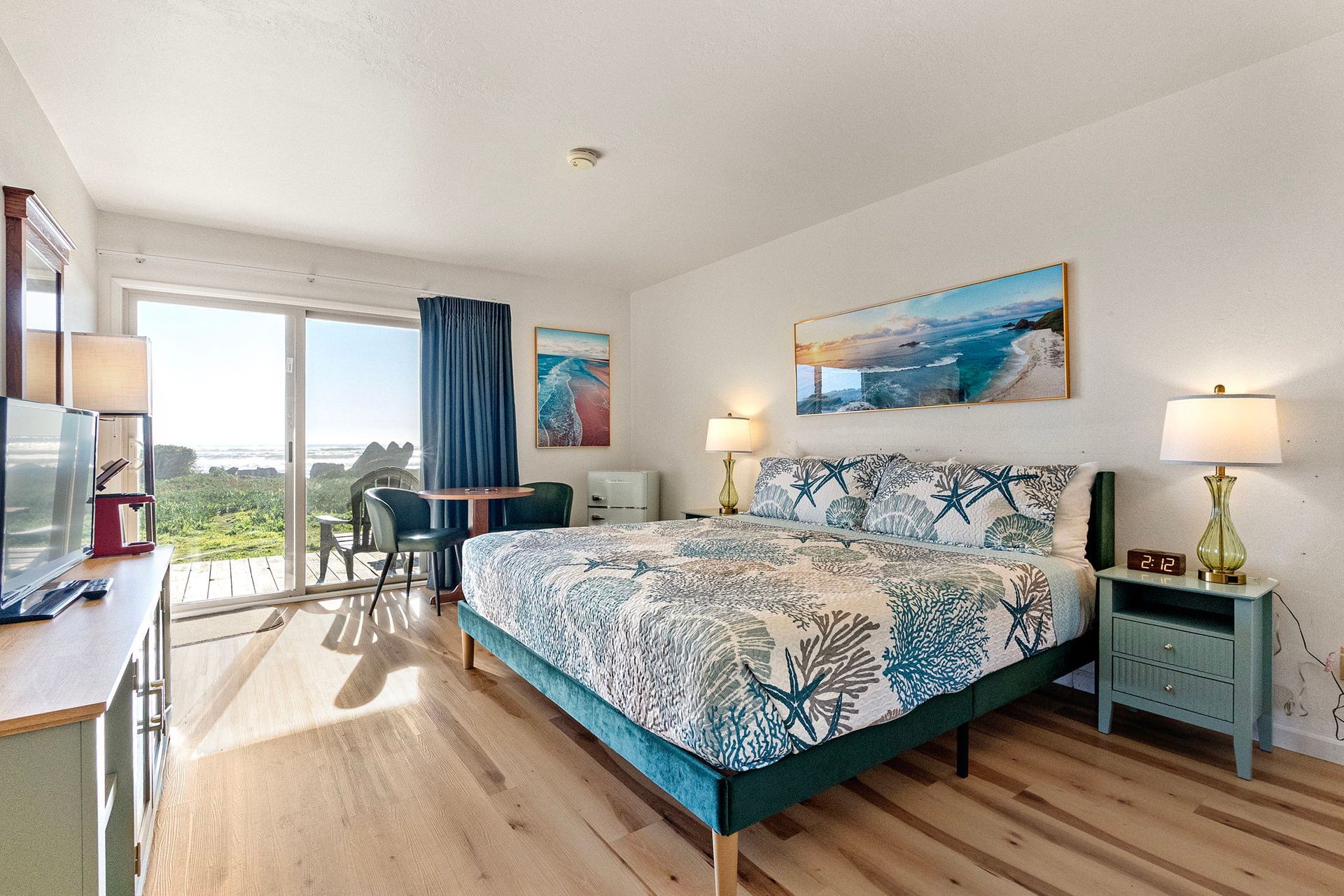 Bedroom with a bed, nightstands, sliding door to ocean view. Beige walls, gray carpet, light.