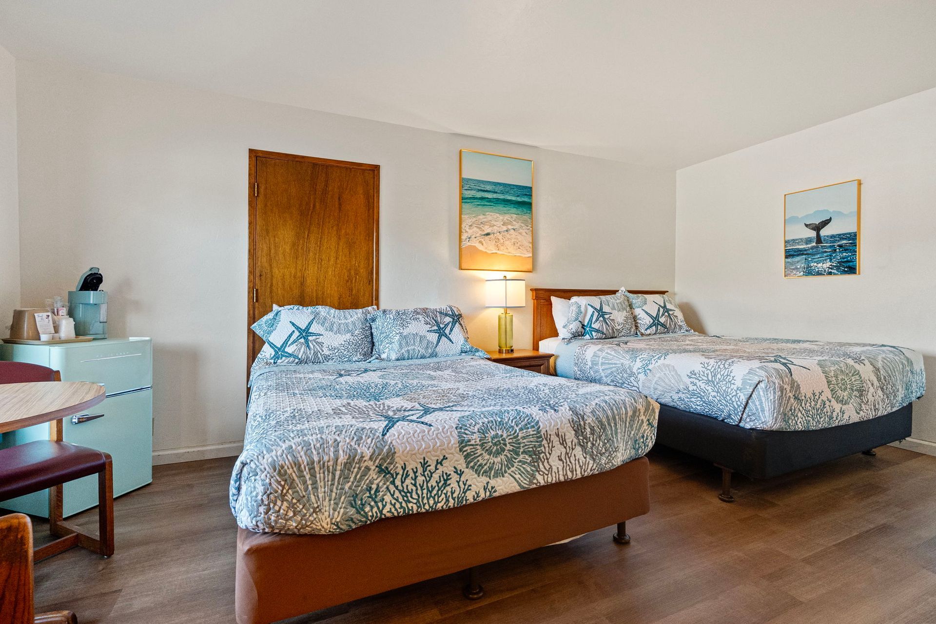 Two beds in a hotel room with two framed pictures and a nightstand between the beds.