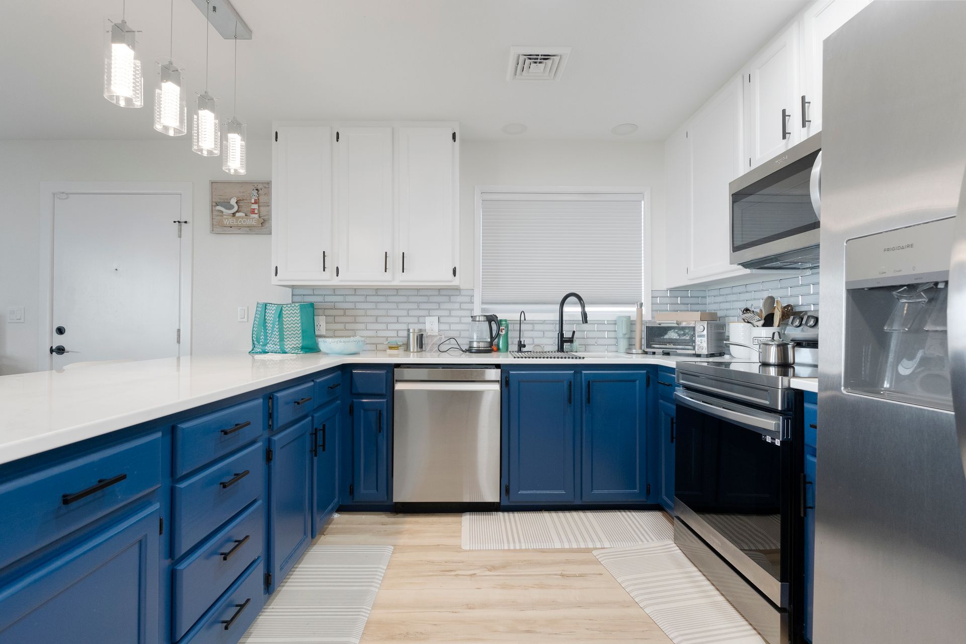 Blue and white kitchen with stainless steel appliances, light wood flooring, and a white countertop.