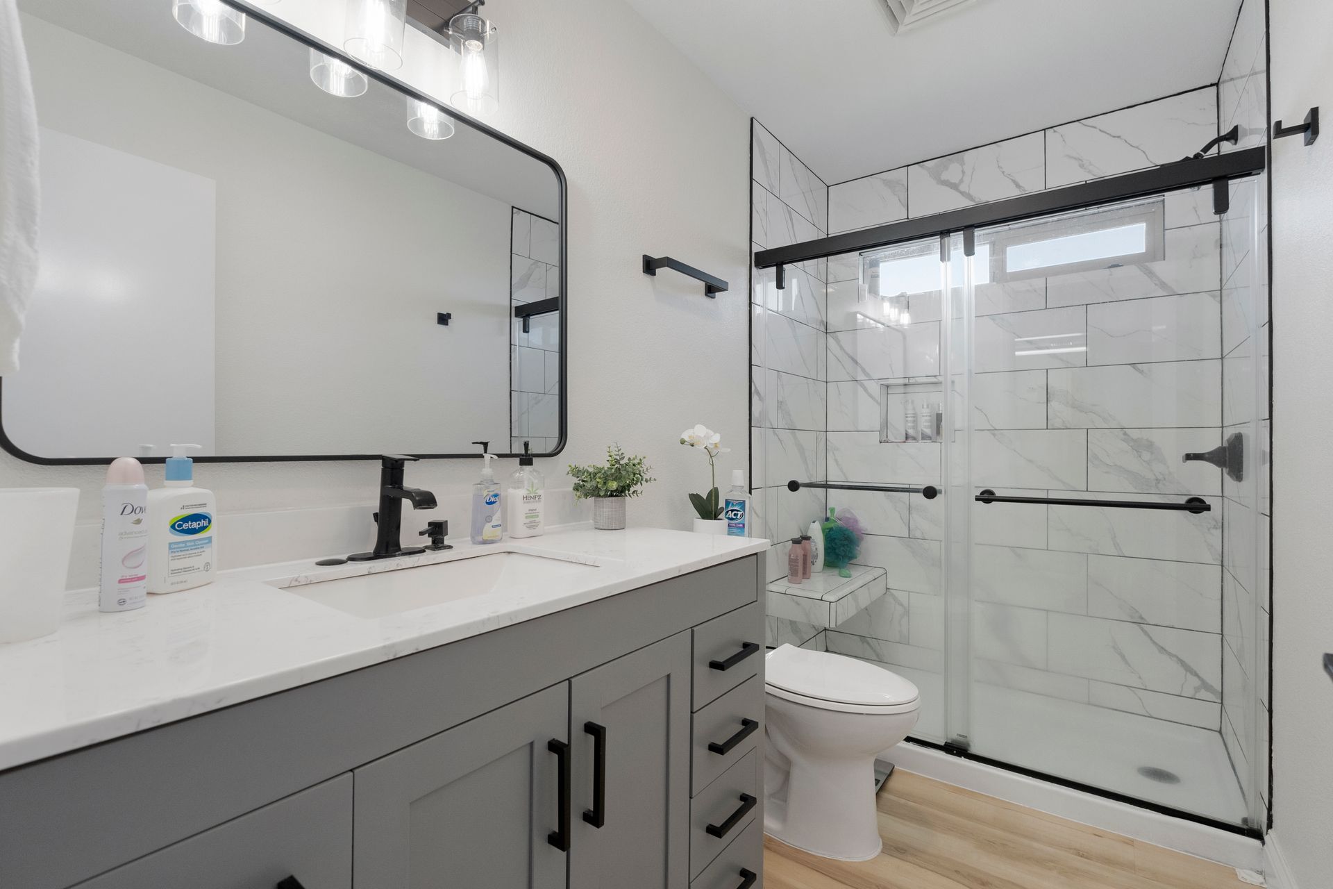 Modern bathroom with gray vanity, white countertop, marble tiled shower, and large mirror.