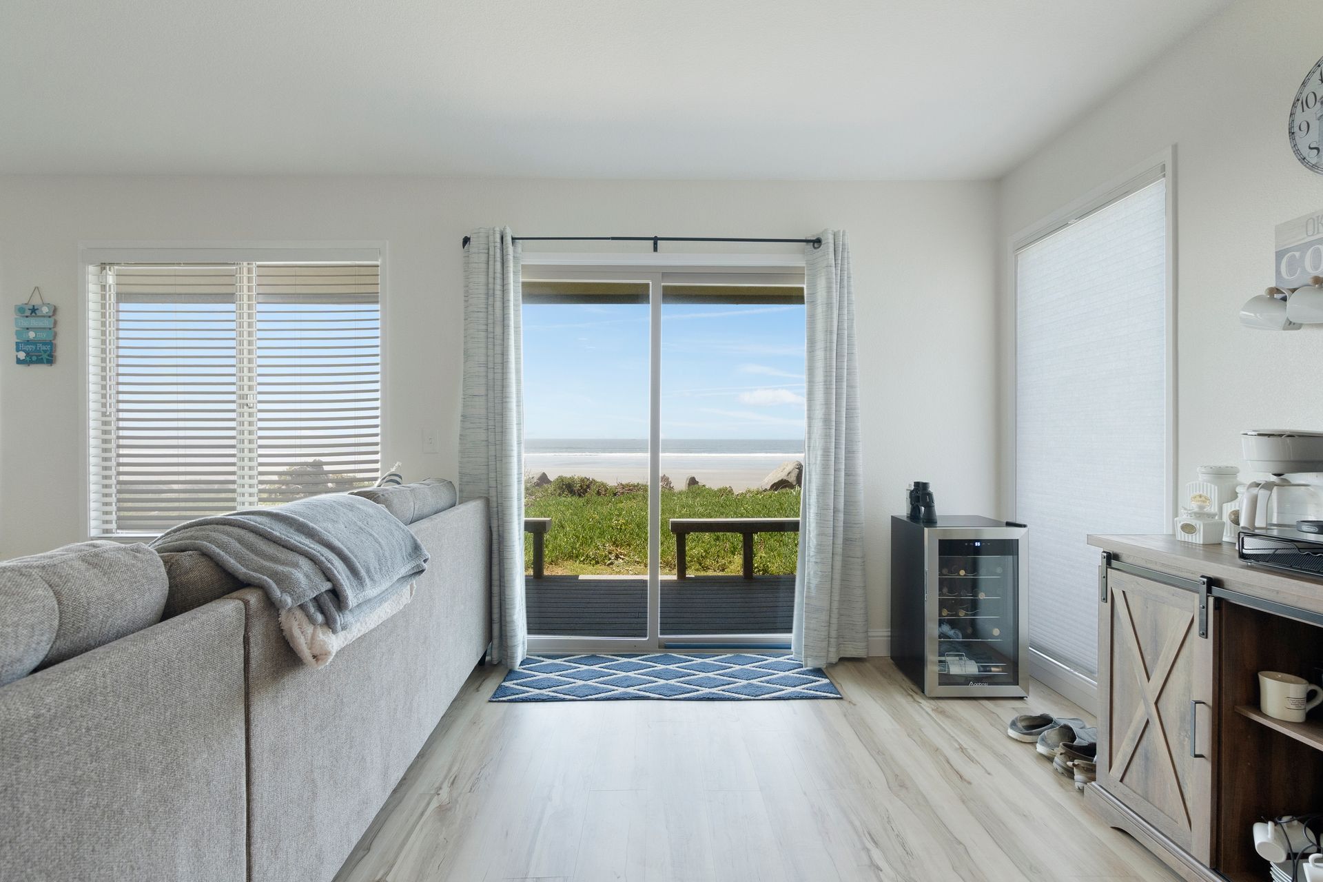 Living room with ocean view through a sliding door, gray sofa, and small wine fridge.